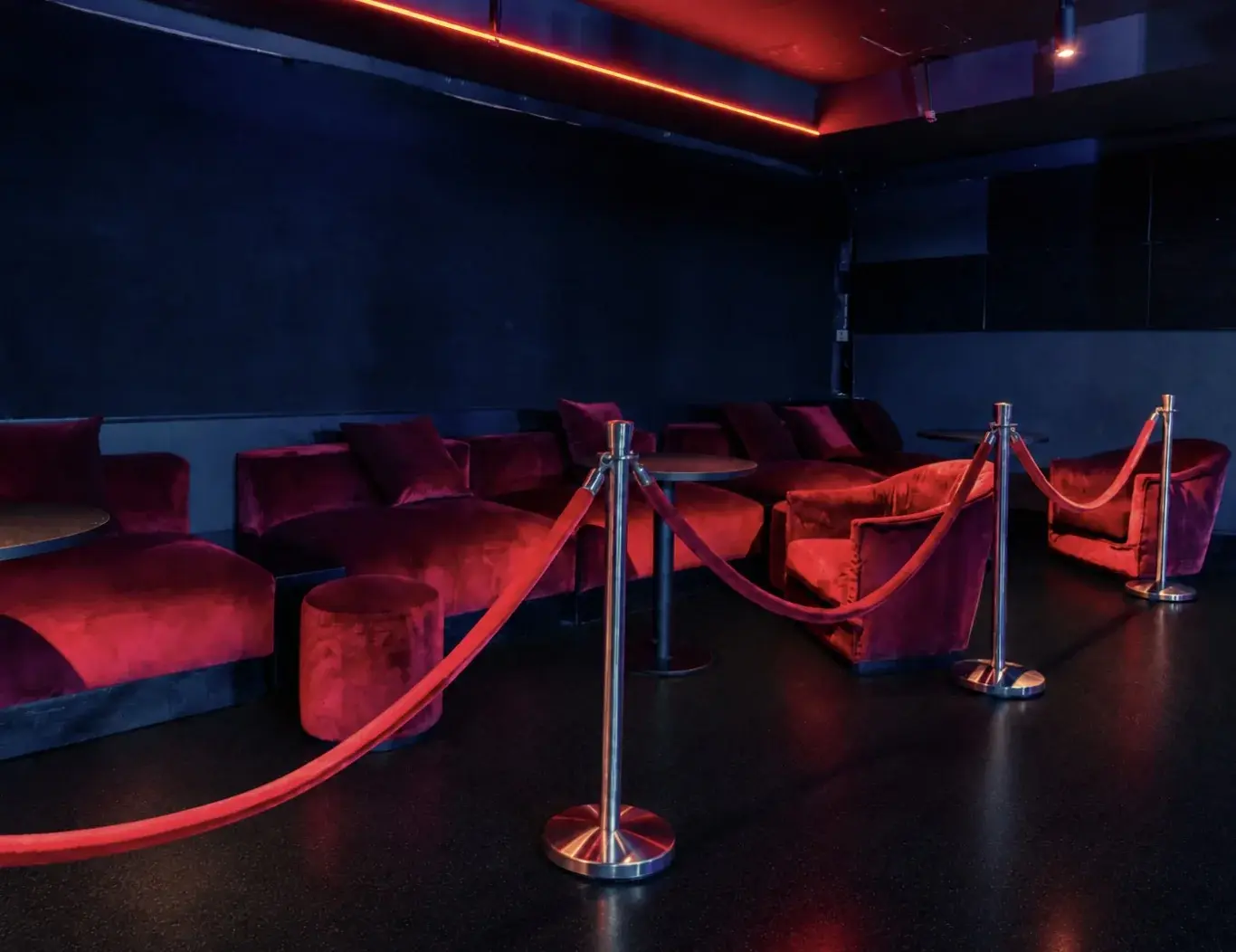 VIP-Bereich mit roten Samtsofas, Kordel und roter Deckenbeleuchtung.